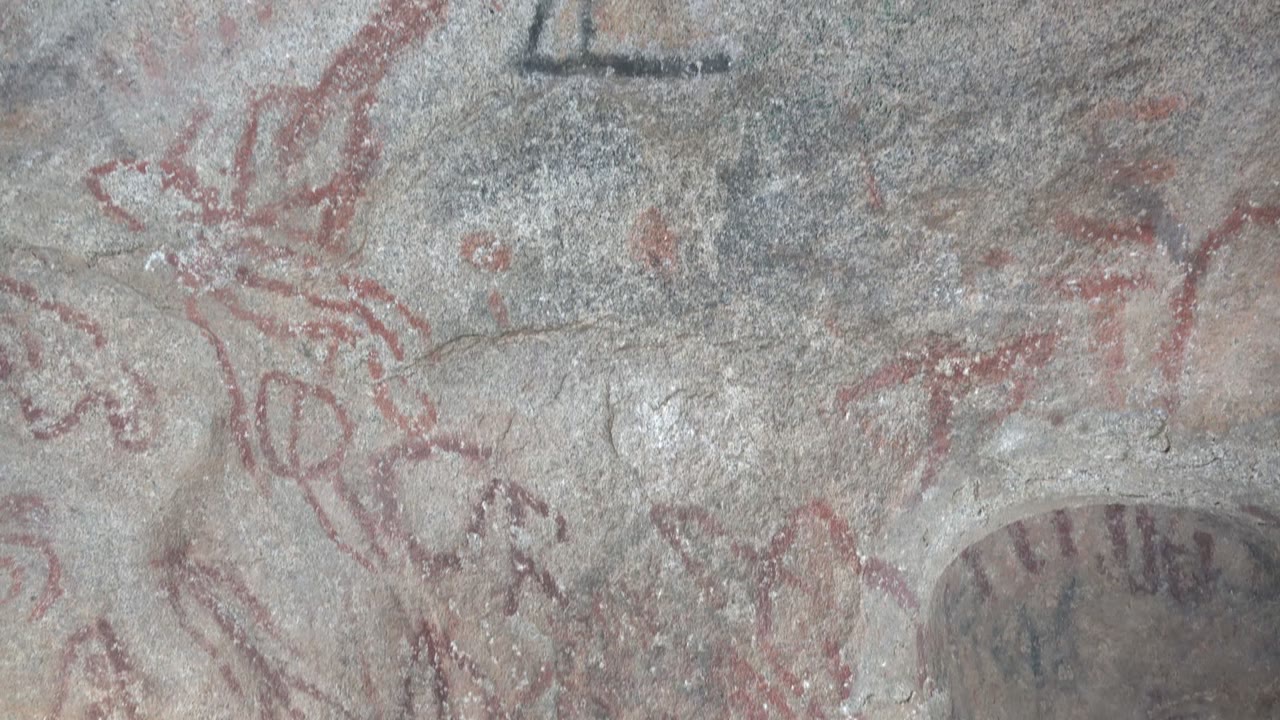 Opening close view of gray rock art in Santa Rosalia, Mexico, with faded red animal-like lines, dark triangular markings, and no visible people.