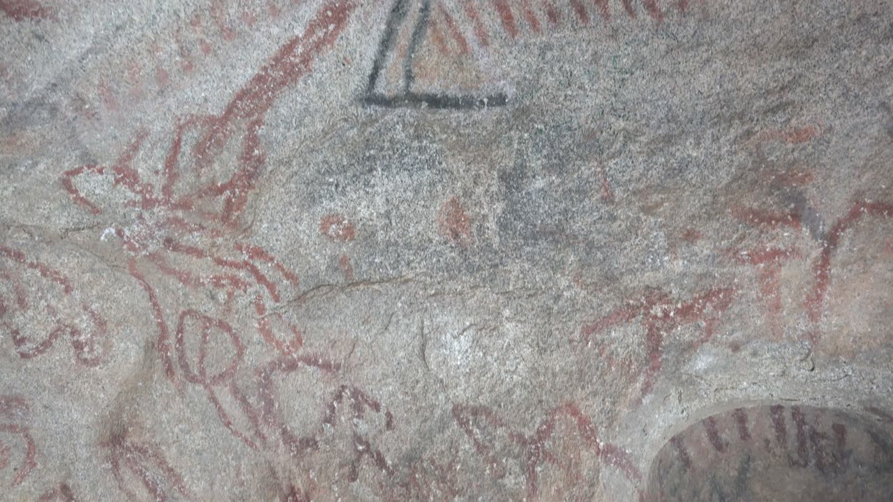 Faded red pictographs and dark marks on gray stone.