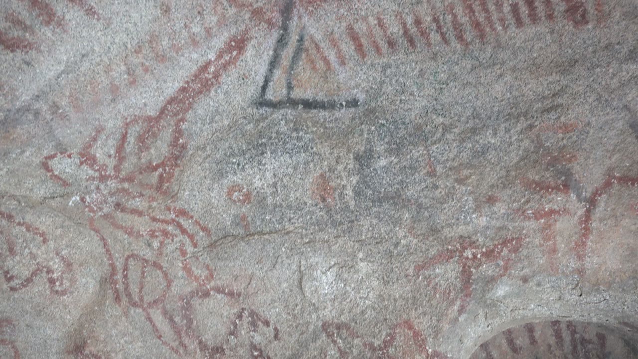 Santa Rosalia pictograph detail with a dark triangular symbol near the upper area, red strokes around it, and no visible people in the tight stone composition.