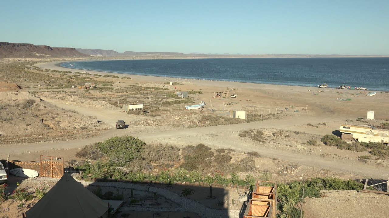 Sandy coastal road with a dark vehicle near the beach and ocean horizon