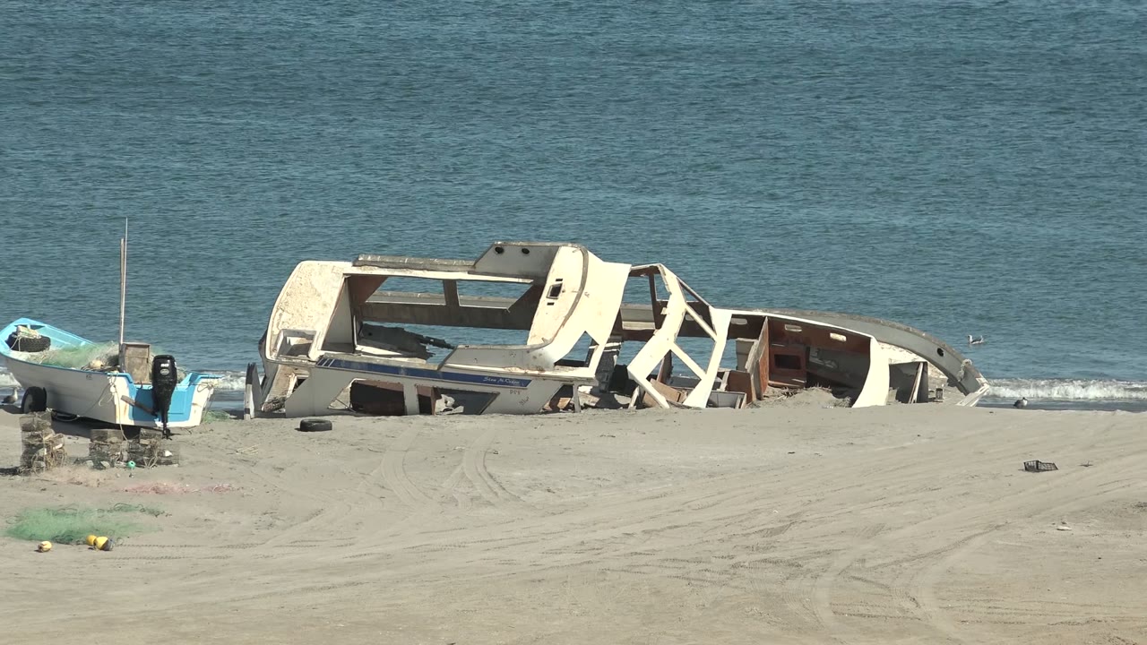 Broken boat hull on sand with ocean behind it