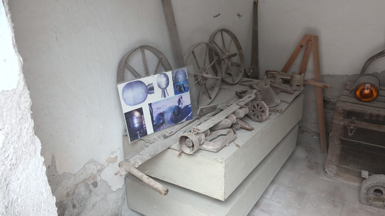 Old tools rest on a white cabinet beside posters, wagon wheels, and a wooden chest.