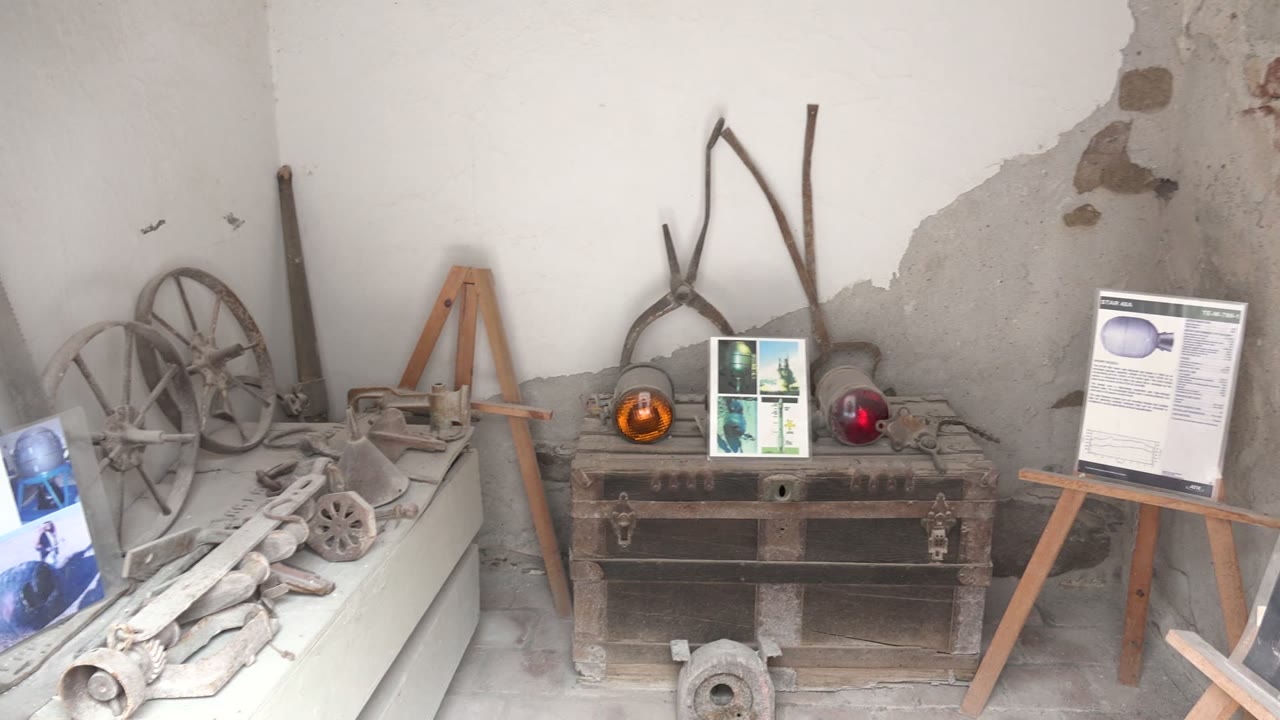 Rustic room in Mulege, Baja California Sur with a white shelf of dusty tools at left, a dark wooden chest in the center, easels with display boards, and no visible people.