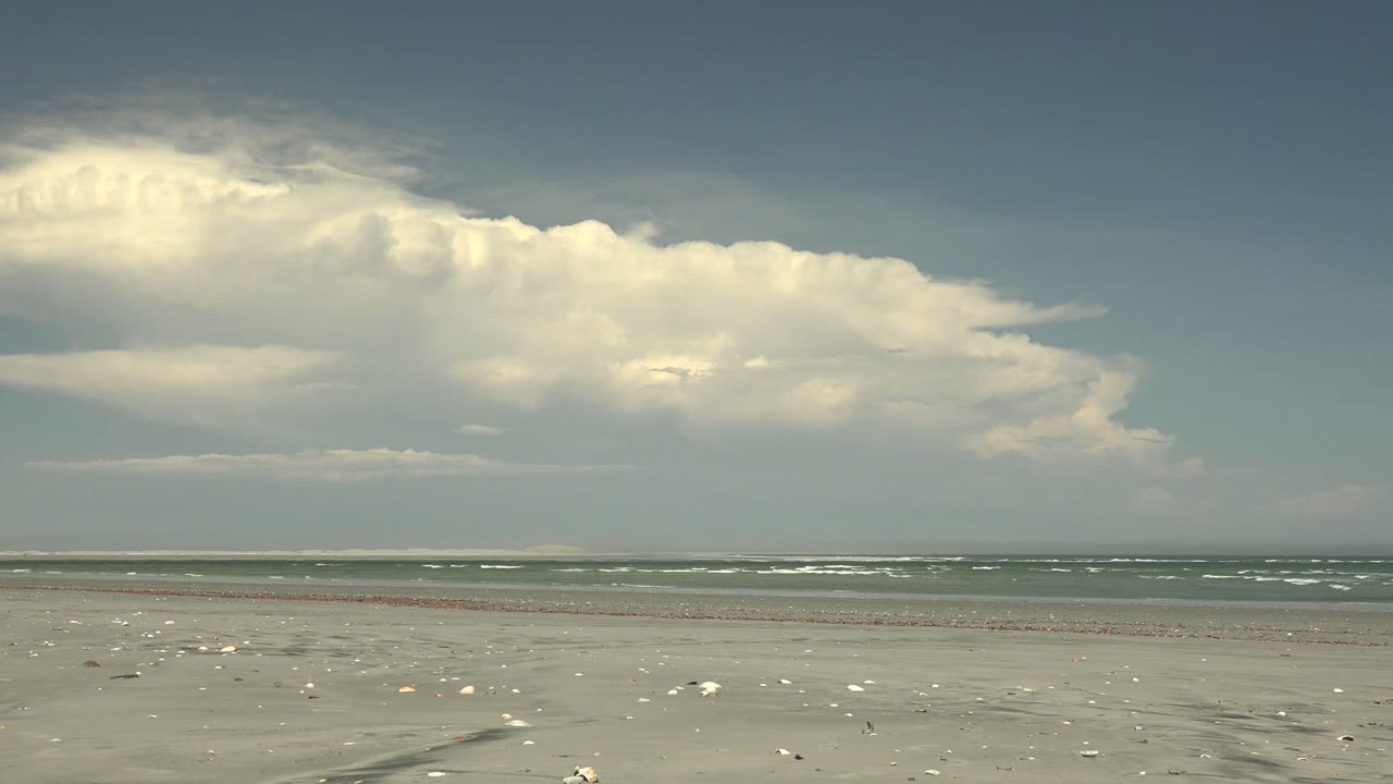 La Bocana beach at 0:02 with shells dotting the sand, distant whitecaps, a darker upper sky, and no visible people.
