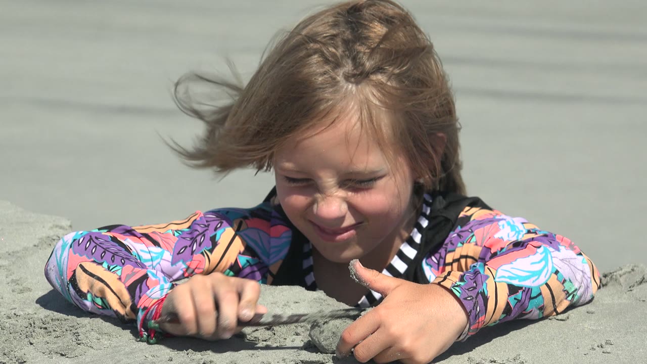 Child squinting in sun while pressing sand with one hand.