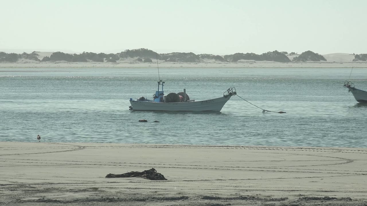 Anchored small boat with another boat farther right on calm coastal water.