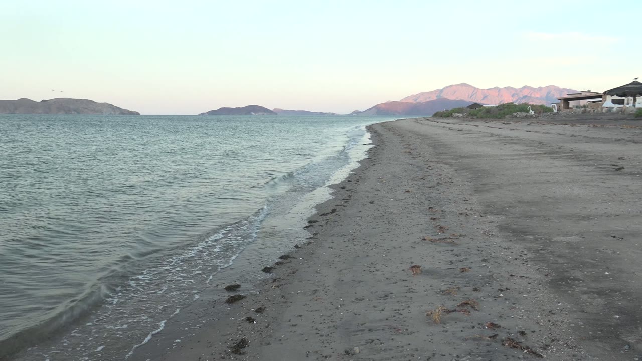 Small wave curling onto sand with islands and pink mountains beyond.