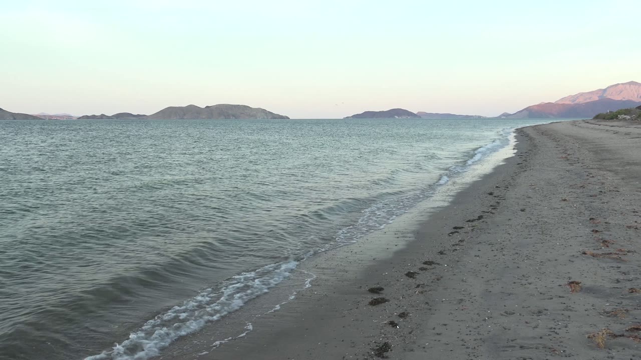 Small wave line reaches the sandy beach with mountains beyond.