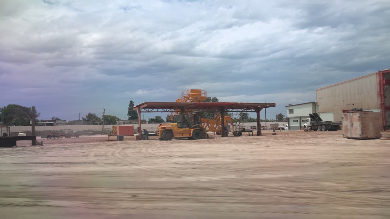 Heavy equipment beside a canopy with open dirt yard in front.