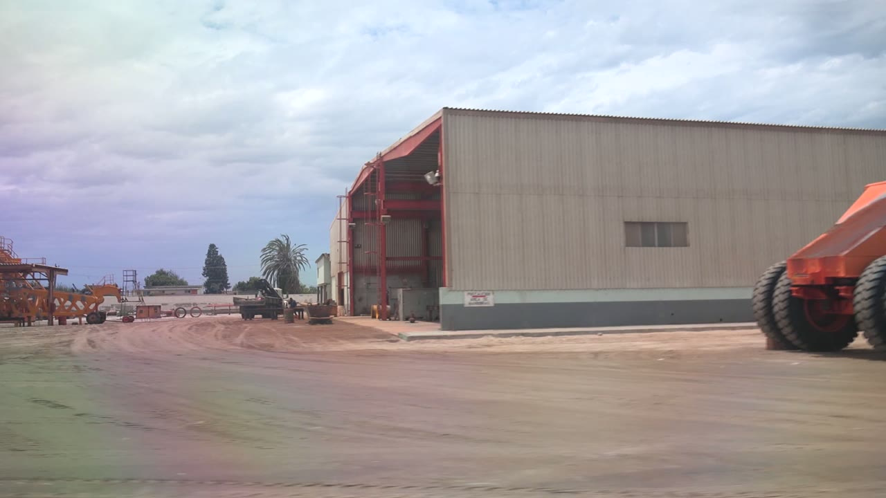 Warehouse bay and orange machinery beside an open industrial lot