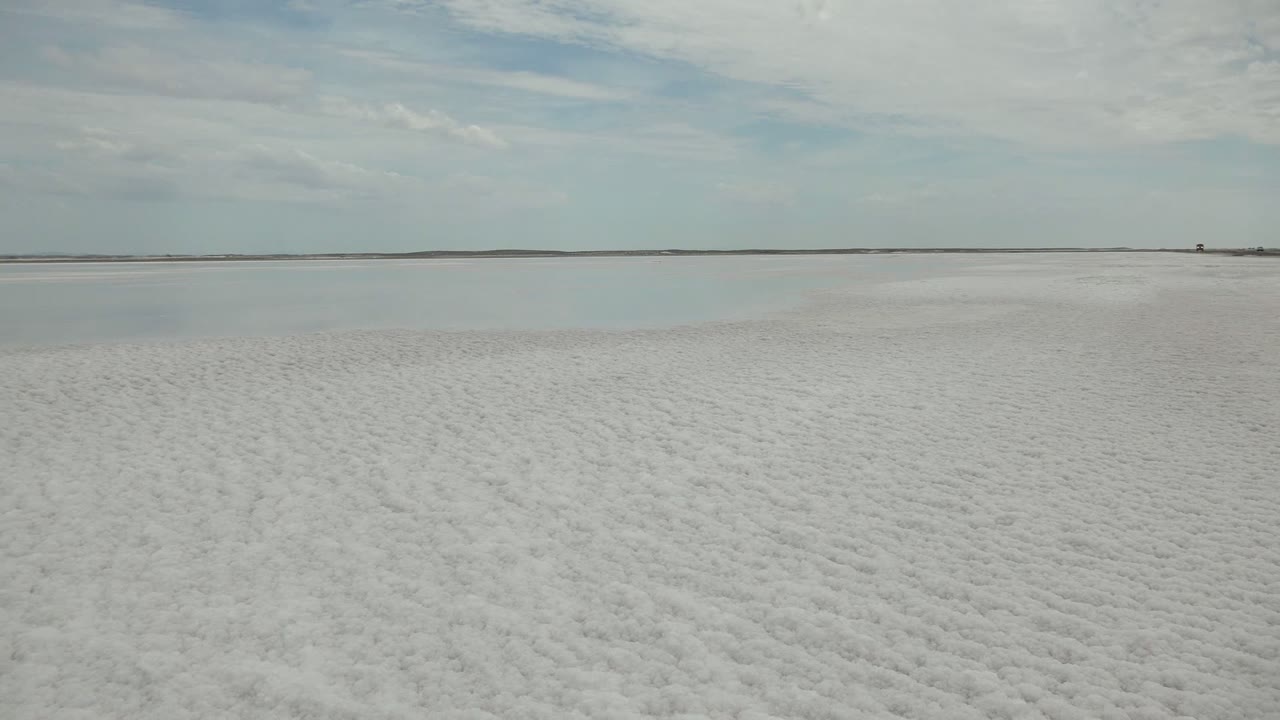 Textured white salt flat leading to still water and a thin horizon.
