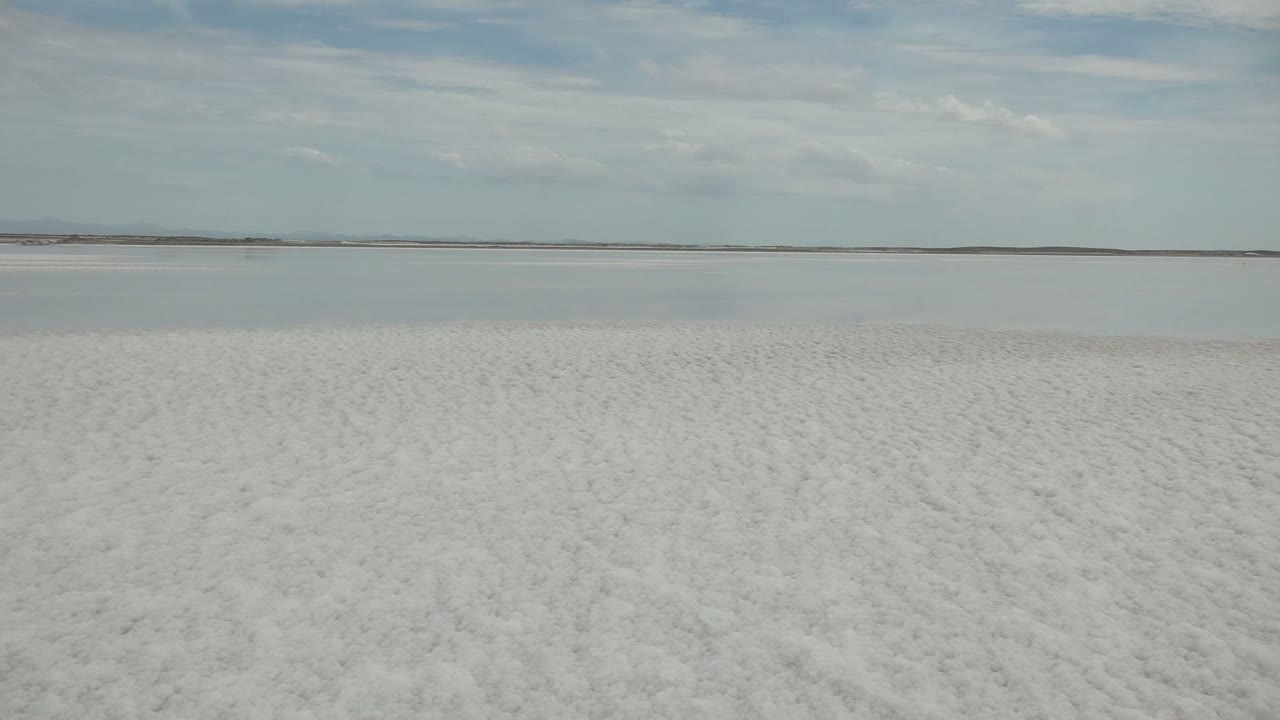 Wide view of a white salt flat in Guerrero Negro, Baja California Sur, Mexico, with a low distant horizon, pale blue-gray clouds, and no visible people.