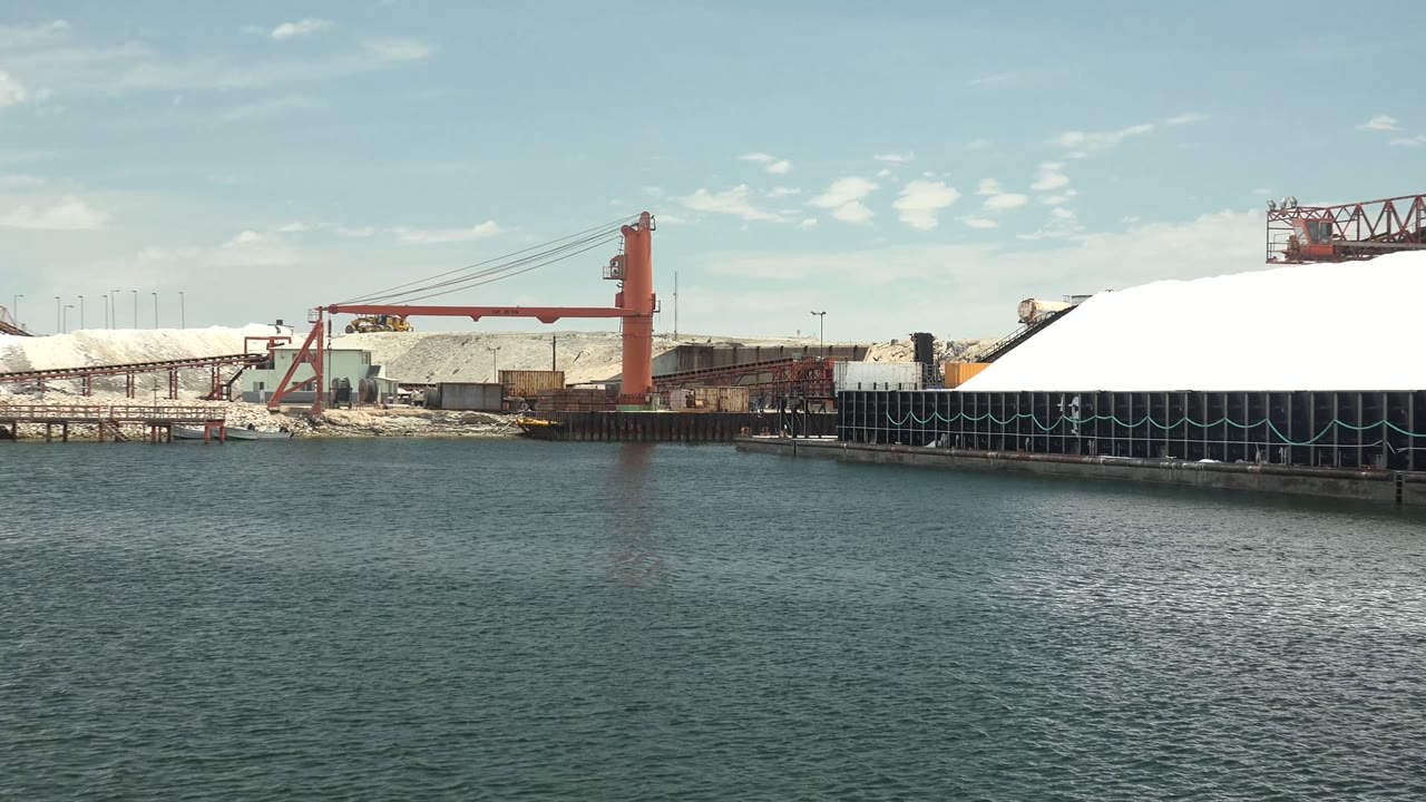 Industrial waterfront with red crane, white piles, dock, and rippled water
