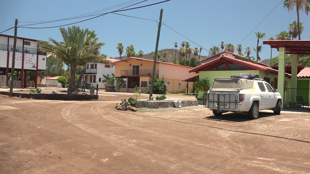White pickup beside a green building on a dusty residential road.
