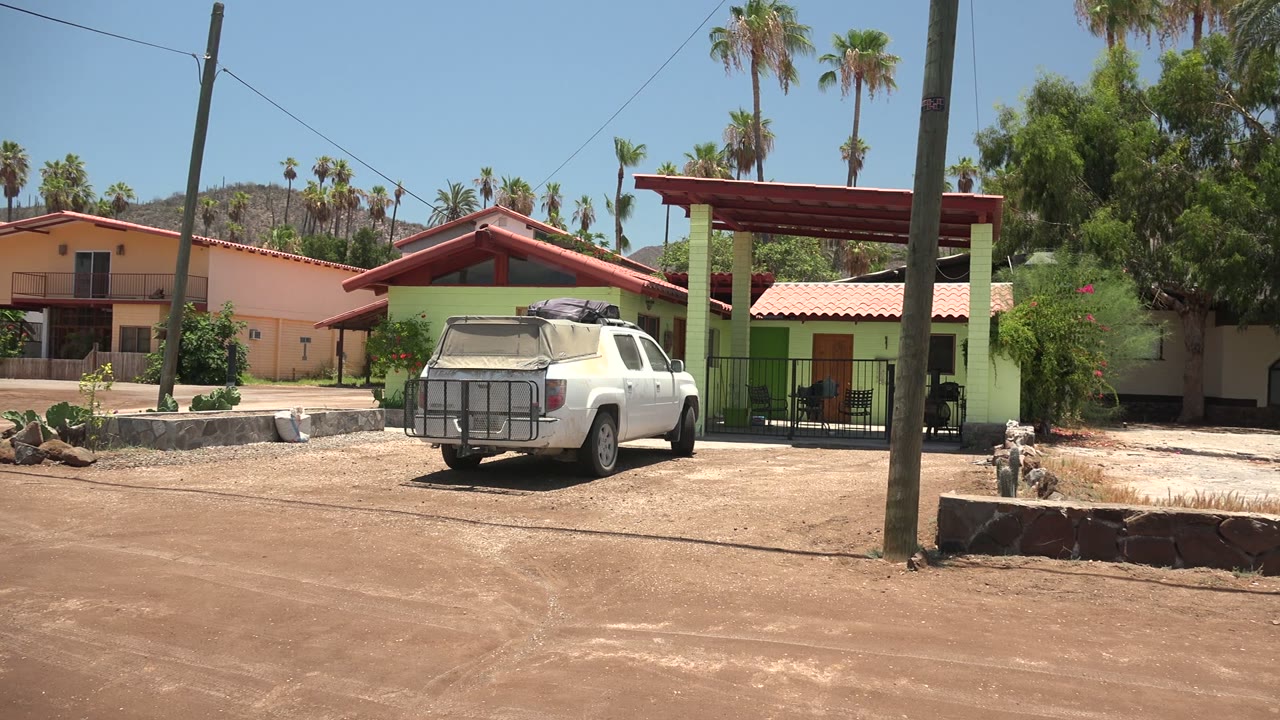Parked white pickup in front of green house with palms behind.