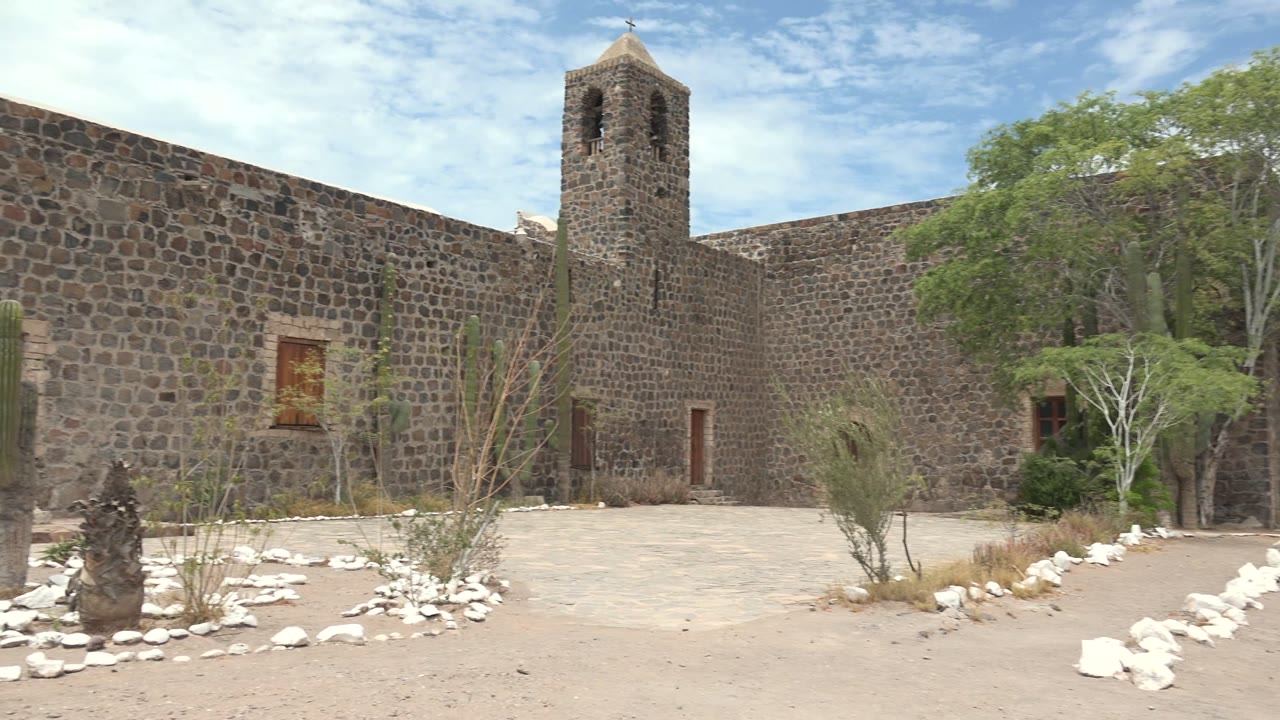 Stone bell tower and courtyard landscaping under a blue sky.