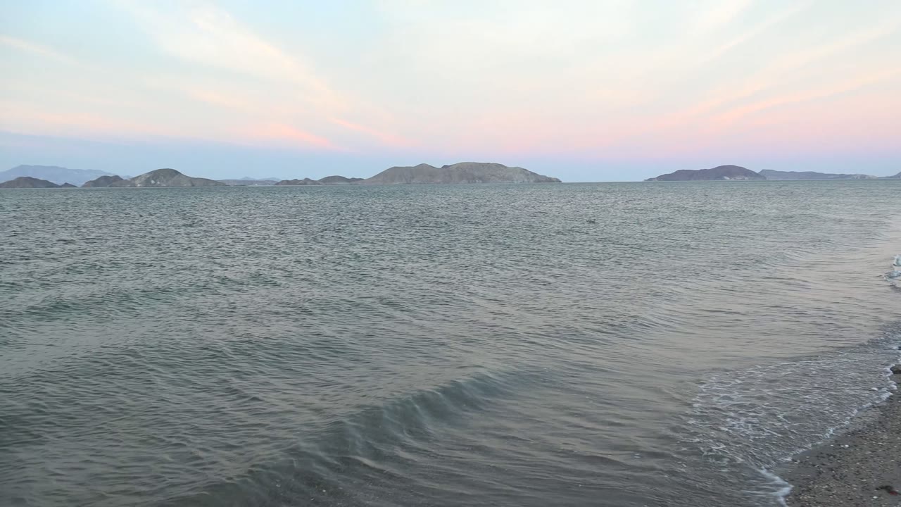 Small wave rolling toward a sandy shoreline with islands in the distance.