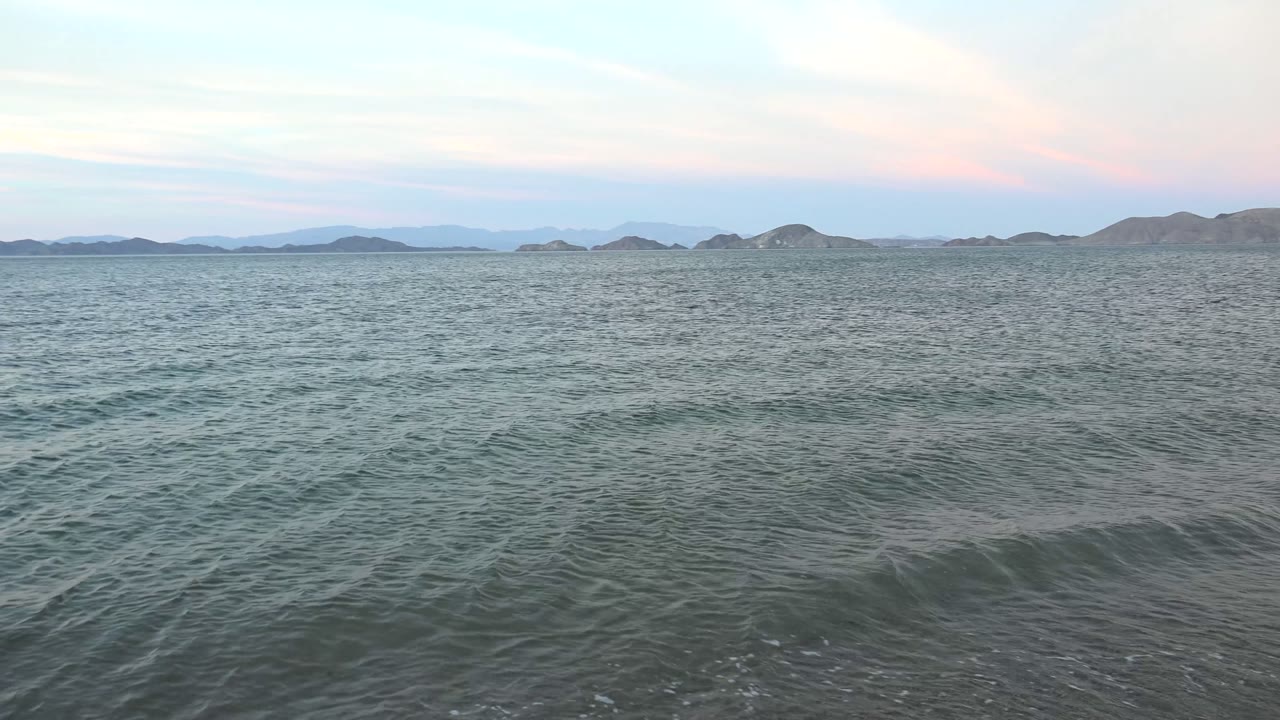 Opening view in Bahia De Los Angeles, Mexico, with rippled ocean water in the foreground, low hills on the horizon, pink and blue sky above, and no visible people.