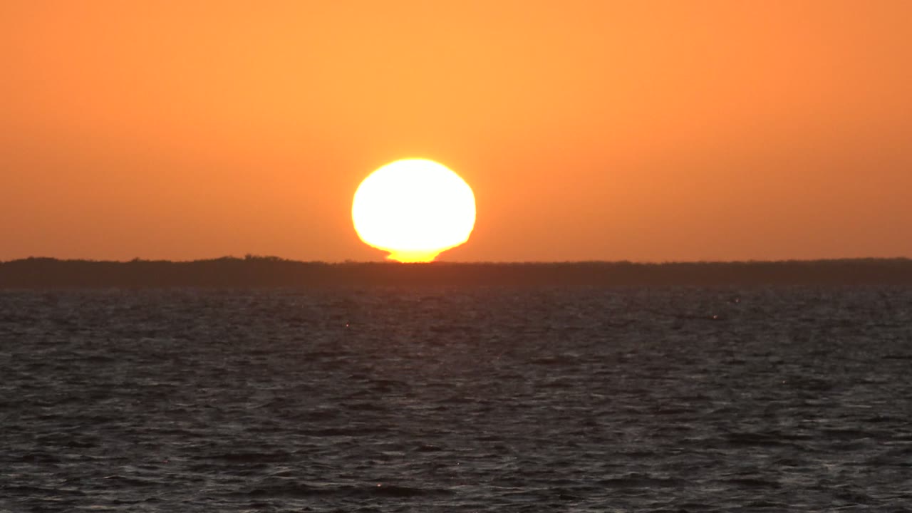 Bright sun near the horizon above dark ocean water.