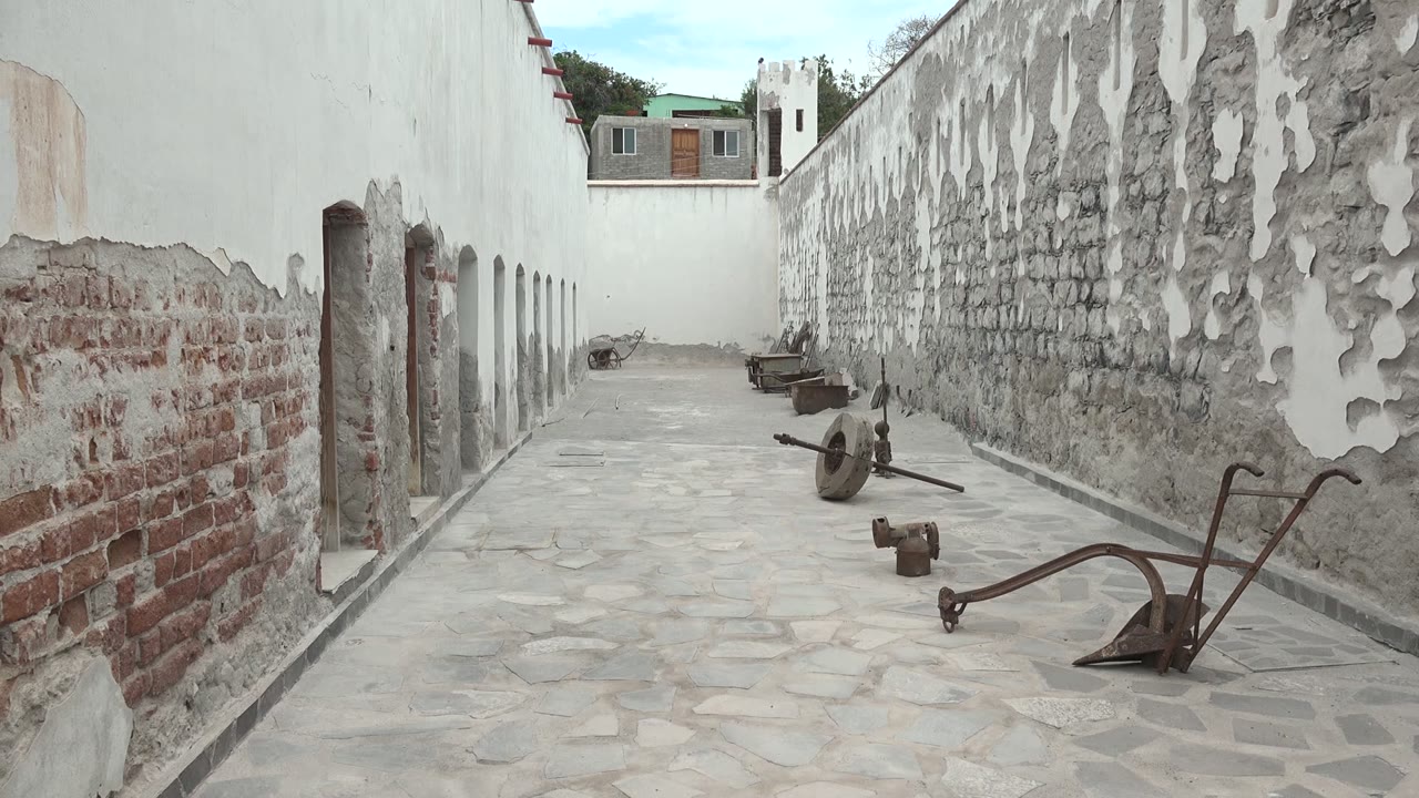 Weathered courtyard corridor with tools lying on stone paving.