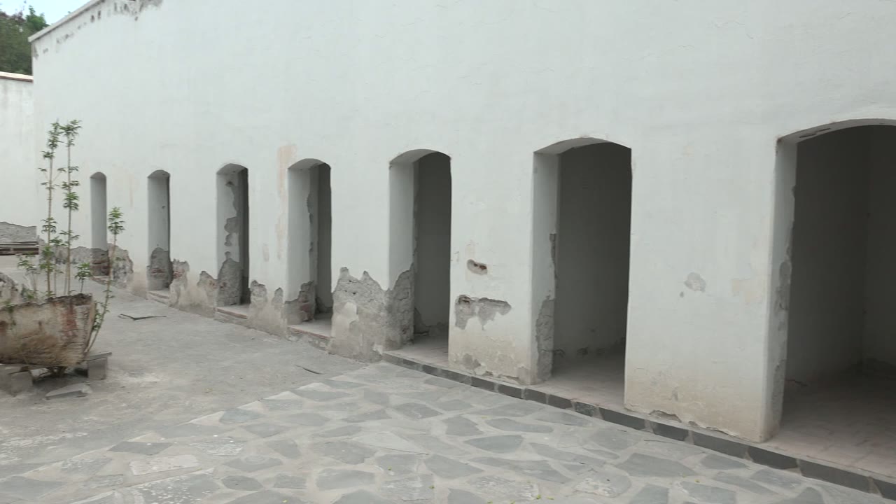 A rusted boat used as a planter sits near the white arched wall of the Mulege courtyard, with greenery above the rear wall and no visible people.