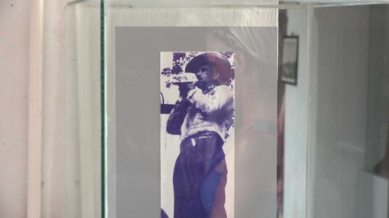 Vintage photo behind glass with wall pipe and reflected person.
