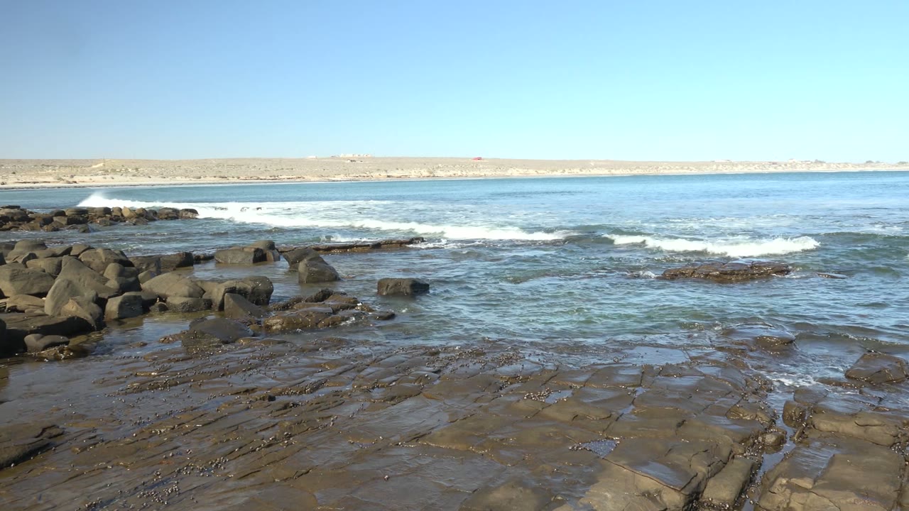Waves roll toward dark rocks with white foam forming offshore.