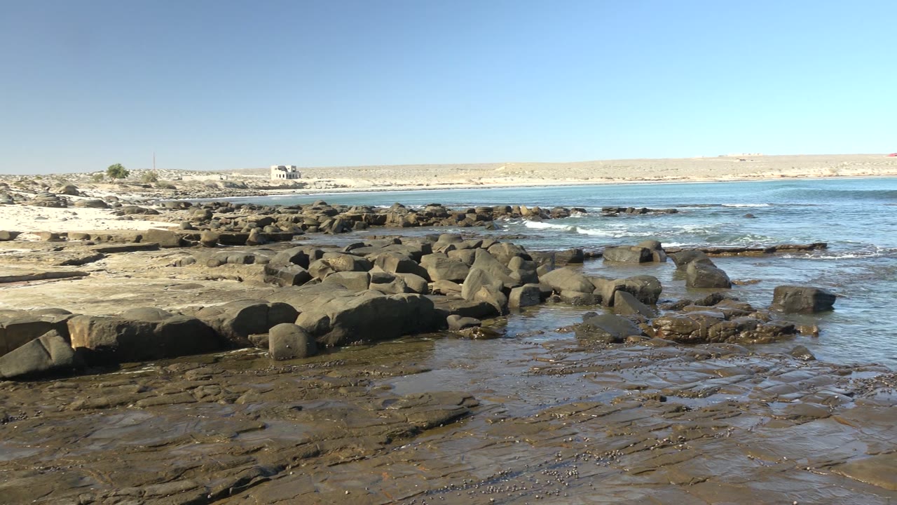 Low surf around shoreline rocks under a clear blue sky.