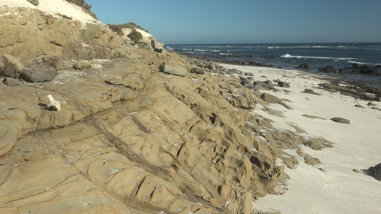 Sandstone shelf beside a sandy beach and breaking waves.