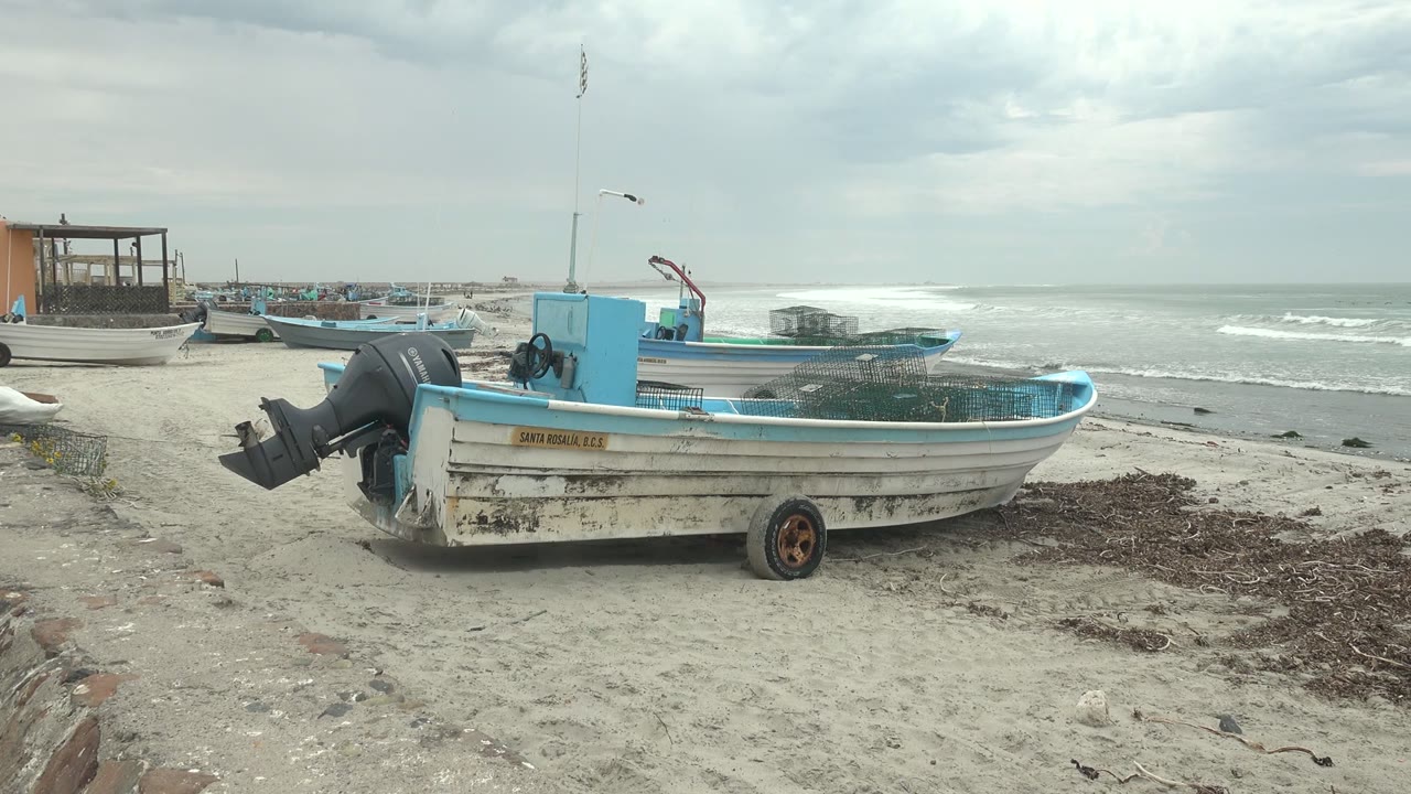 Fishing boat with outboard motor on sand under cloudy sky.