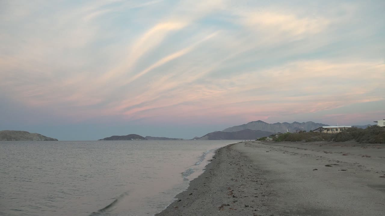 Calm ocean beside a sandy beach under pink and blue sky