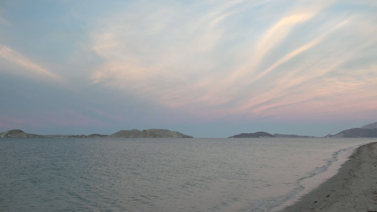 Calm water and low islands under broad pink and cream cloud streaks.