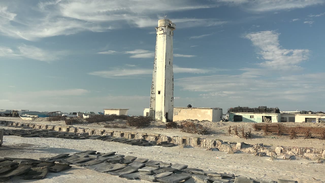 Lighthouse above beach rocks with small buildings in background