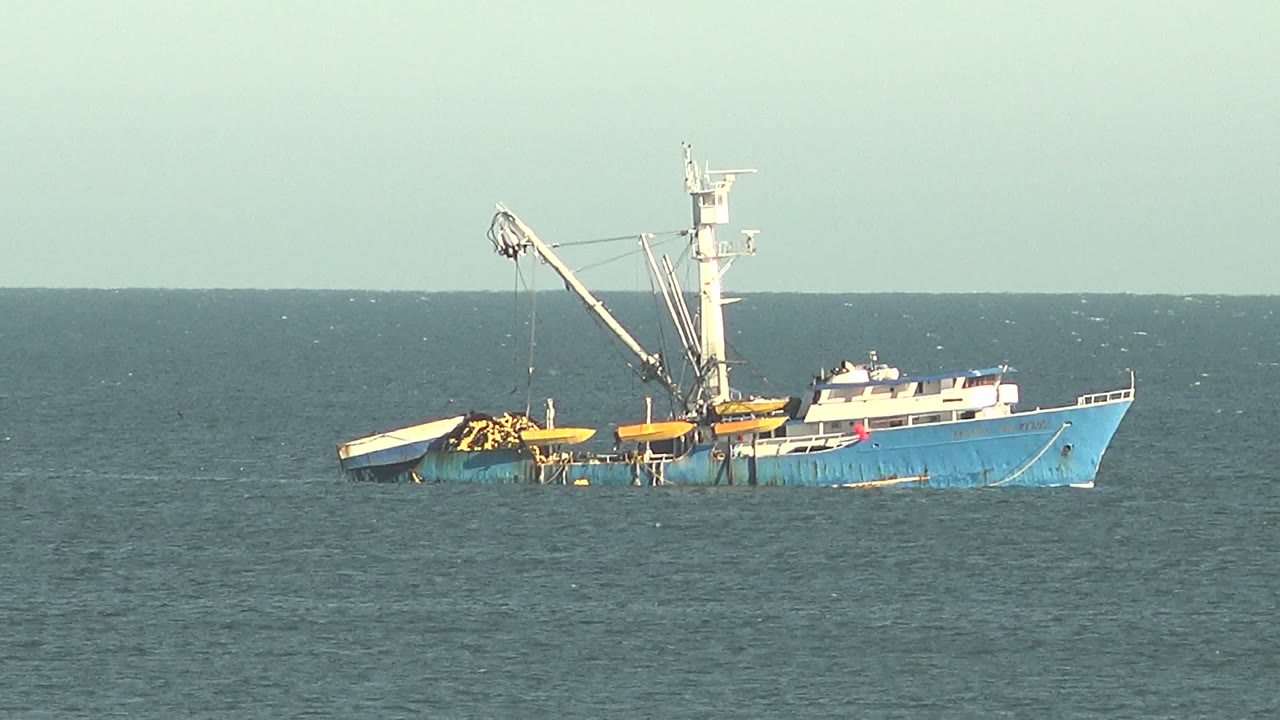 Blue fishing vessel with a crane and yellow deck gear floats on open water near San Juanico, Baja California Sur, with no visible people.