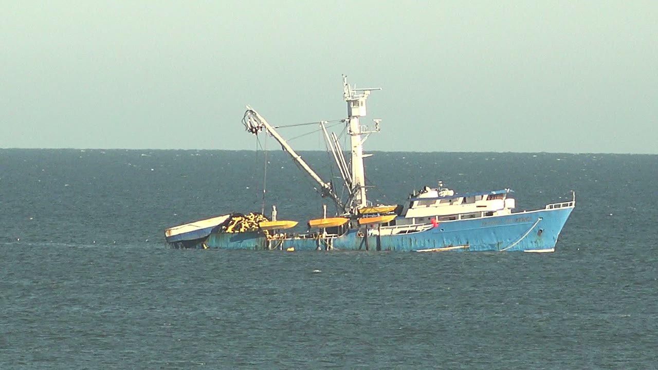 Fishing vessel with tall crane and yellow equipment at sea.