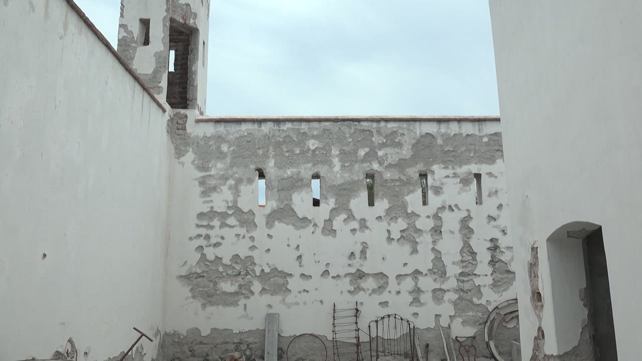 White courtyard wall and crenellated tower with peeling plaster.