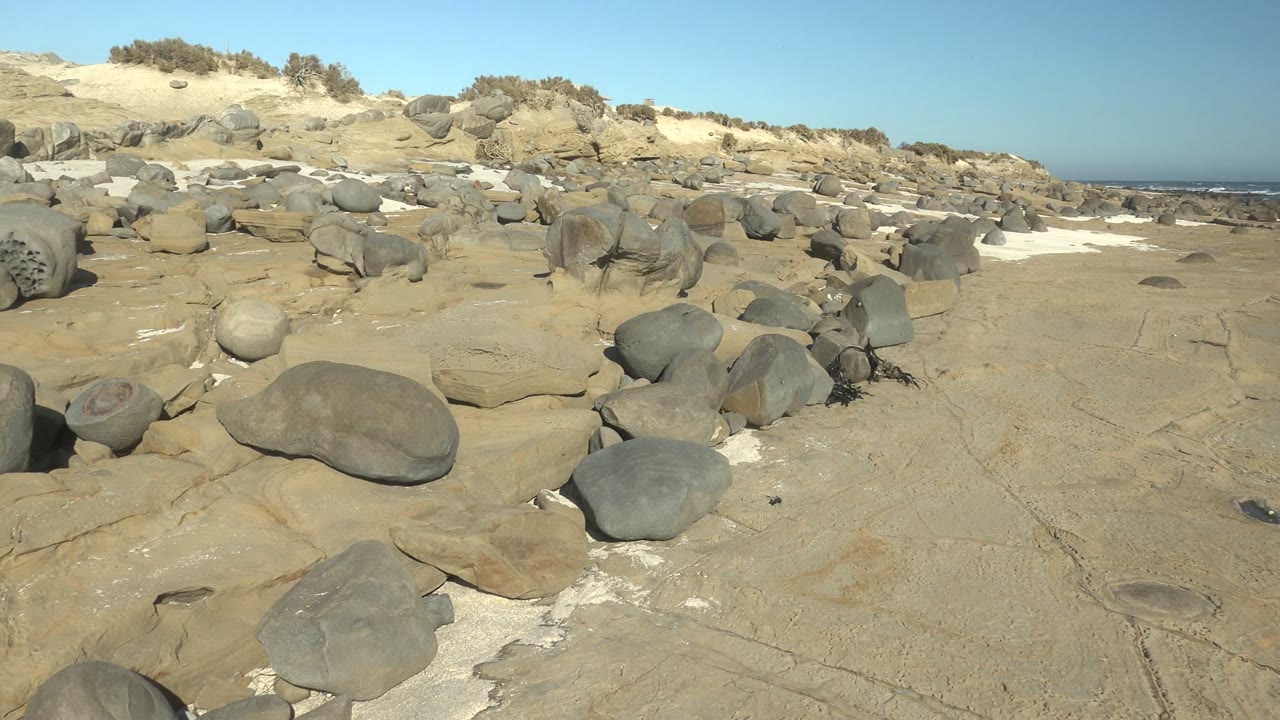 Smooth rocks and sandy shoreline with a faint ocean horizon to the right.