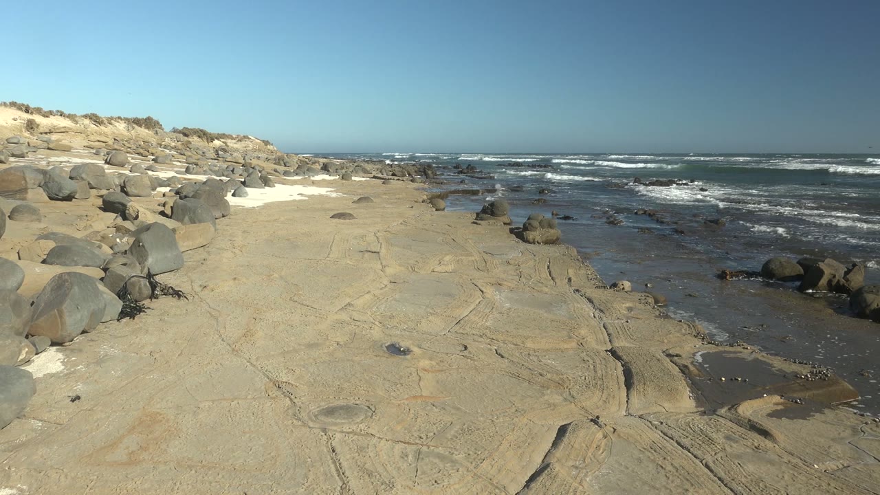 Pale rock shelf with waves breaking beyond wet shoreline pools.