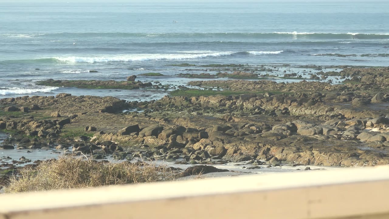 Rocky shoreline and waves with a pale railing at the bottom