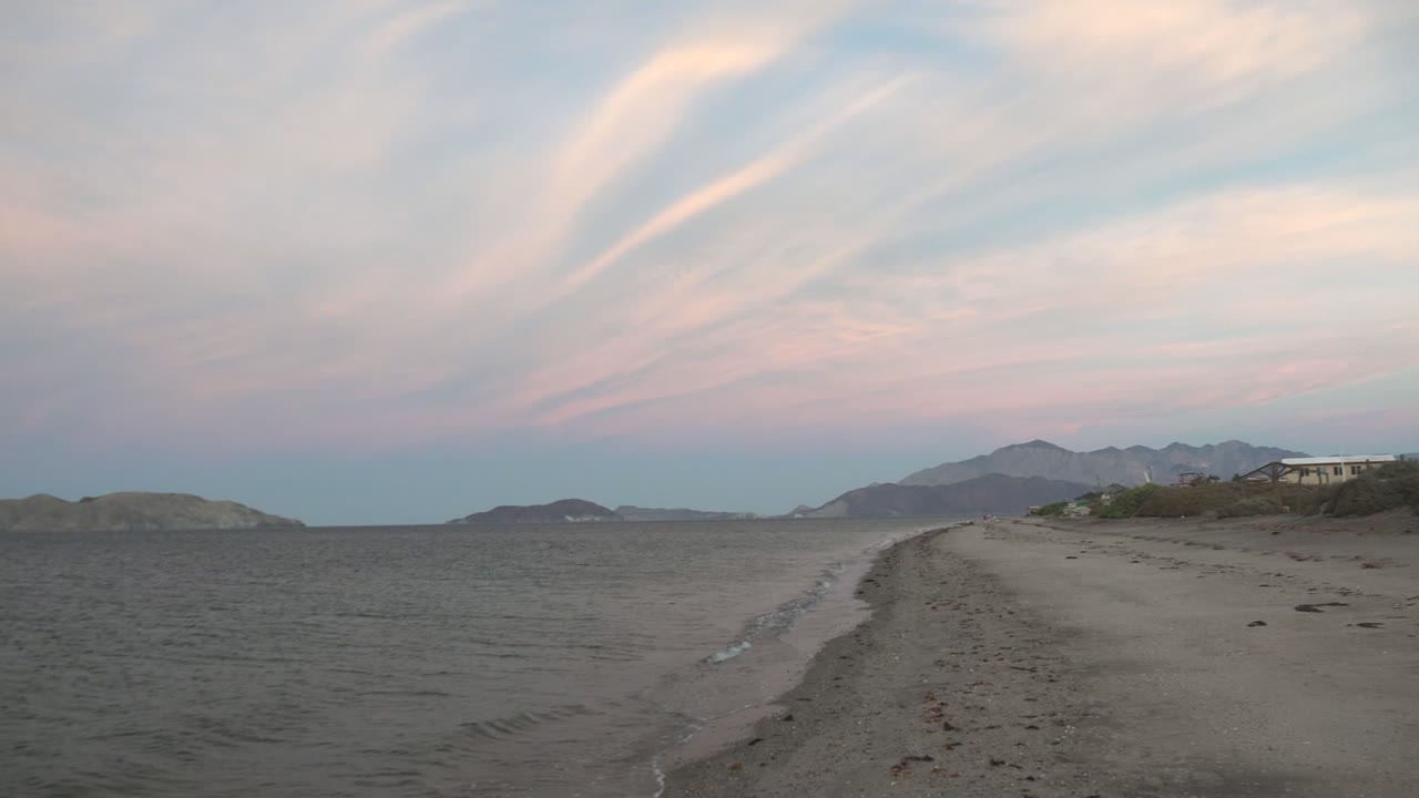 Curving sandy shore with gentle wave wash and distant mountains at dusk.