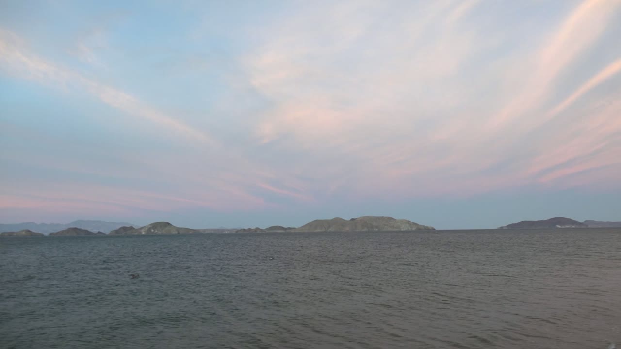 Bahia De Los Angeles ocean frame with textured water in front, a chain of distant islands across the horizon, pale blue sky, pink clouds, and no visible people.
