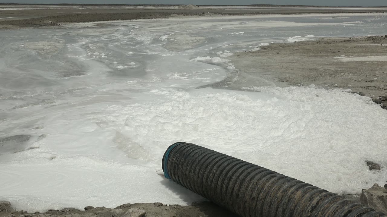 Foam spreading around a large pipe at the edge of shallow water.