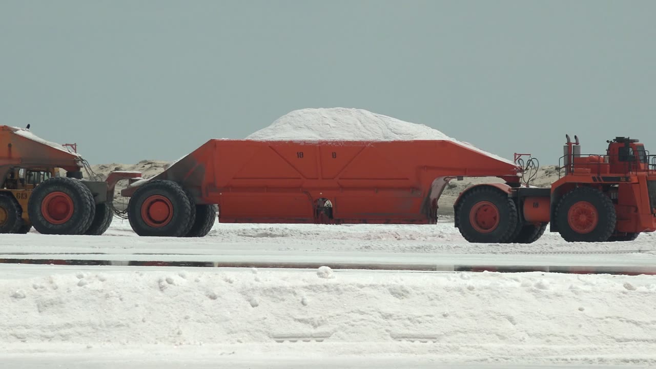 Long red haul trailer with white material moving across the flat.