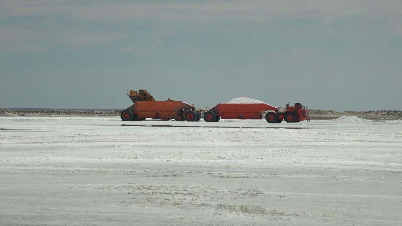 A wide view in Guerrero Negro, Baja California Sur shows red industrial vehicles and a covered red trailer on a white flat field, with no visible people.