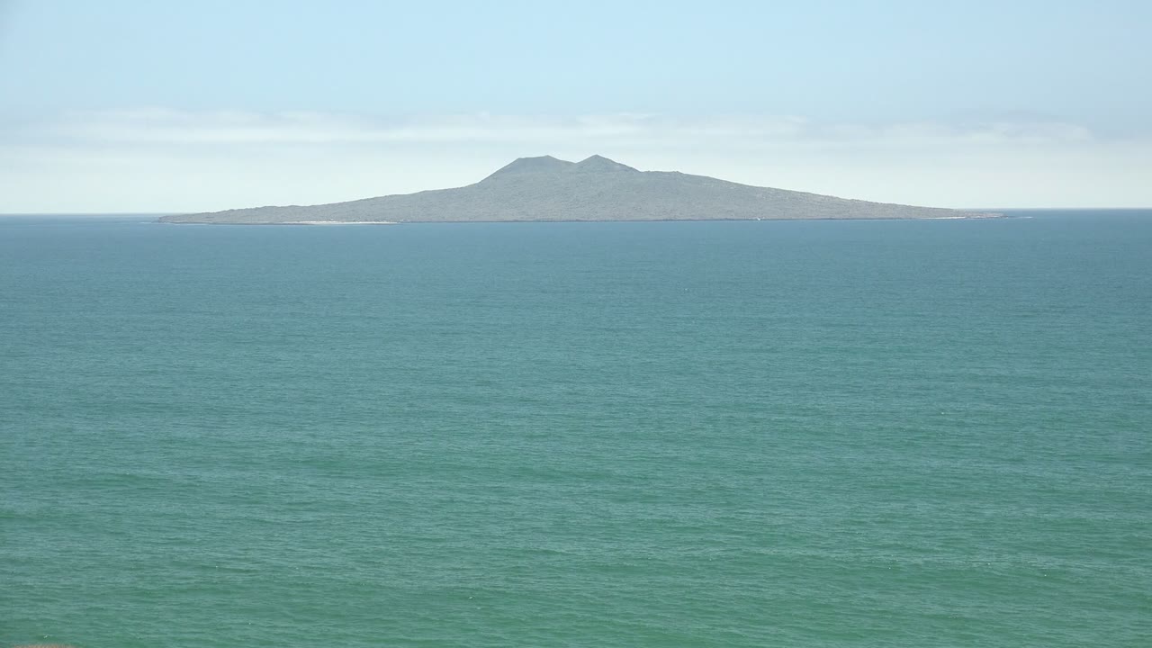 San Quintin BC Mexico ocean view at the start of the clip, with a distant island on the horizon, blue-green water in the foreground, light clouds above, and no visible people.