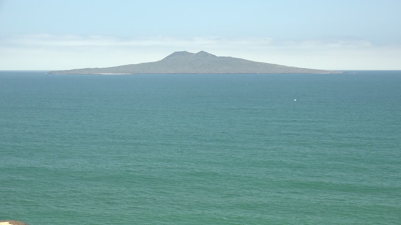 Wide San Quintin BC Mexico ocean view at the start of the clip, with a distant mountain island on the horizon, faint boat specks on the water, and no visible people.