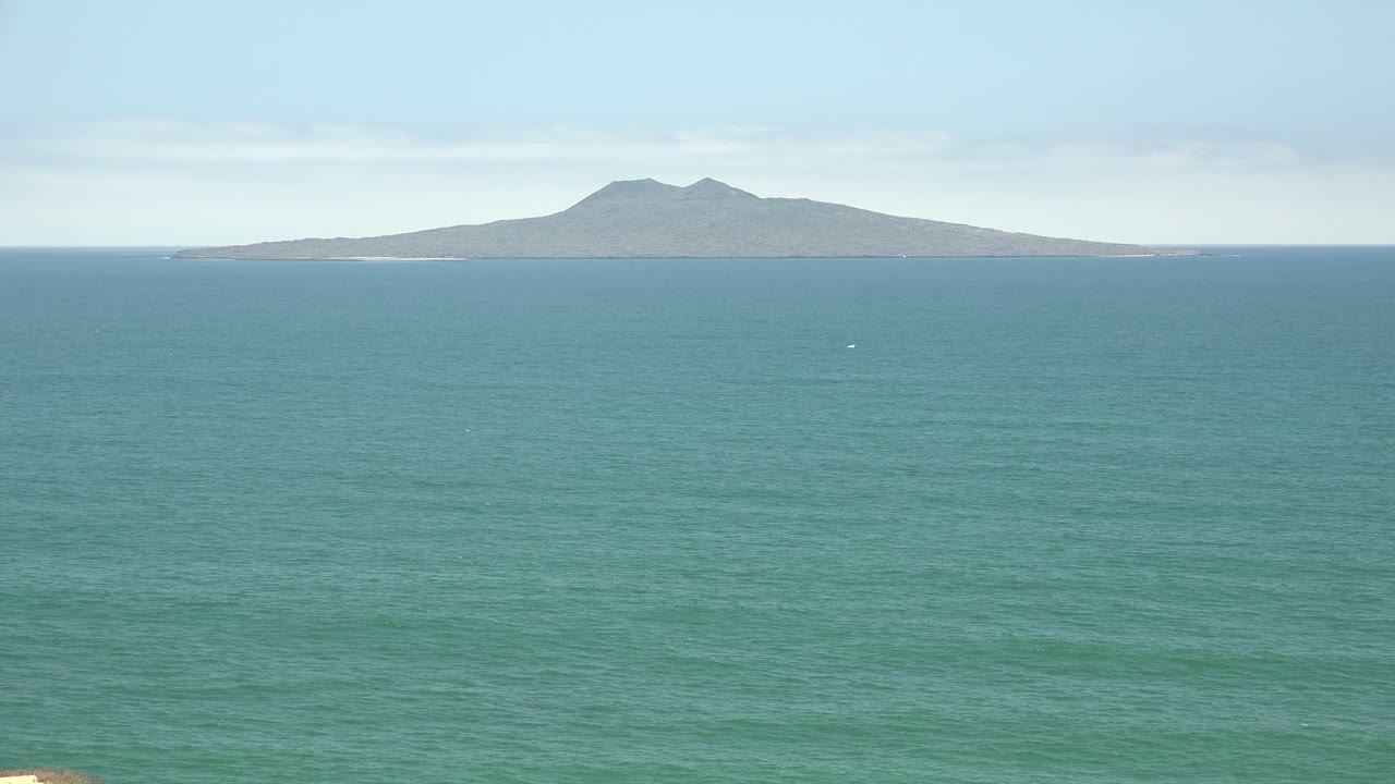 Calm ocean with a low island and mountain ridge on the horizon.