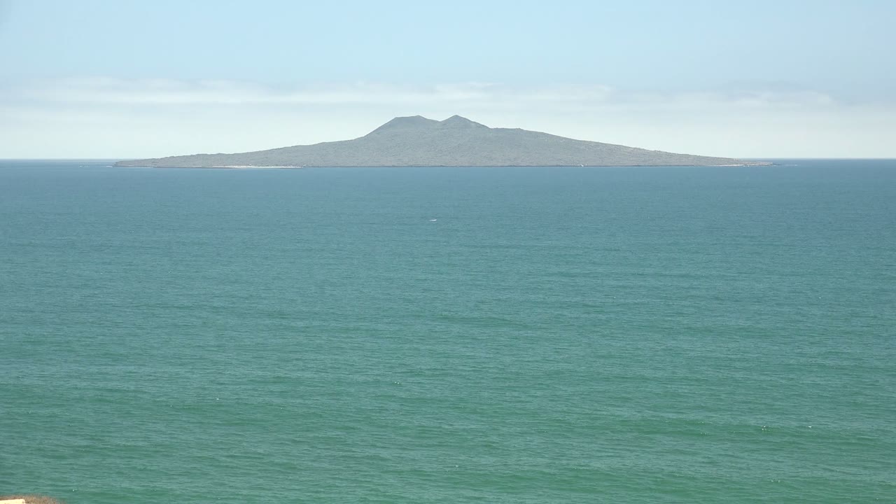 At 0:02, the San Quintin BC Mexico horizon remains steady, with a small white boat speck more noticeable against the open water beneath the distant mountain island and no visible people.