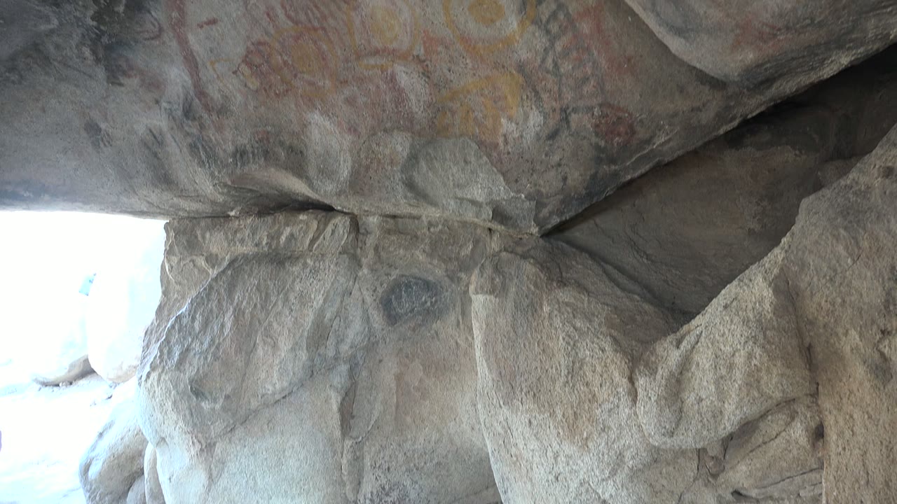 Start of the Santa Rosalia cave ceiling pan, showing rough gray rock, faded red and yellow pictographs, a bright cave opening at the lower left, and no visible people.