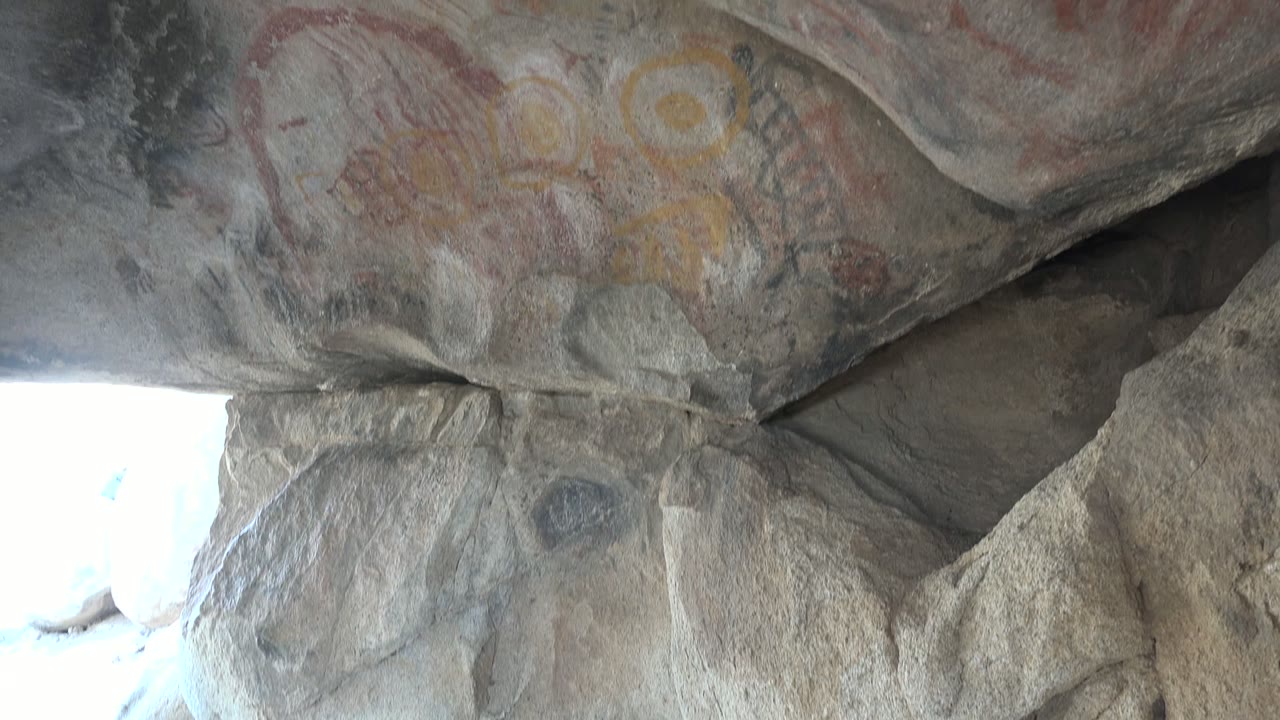 Rock ceiling with red line pictographs and yellow circular markings near a cave opening.
